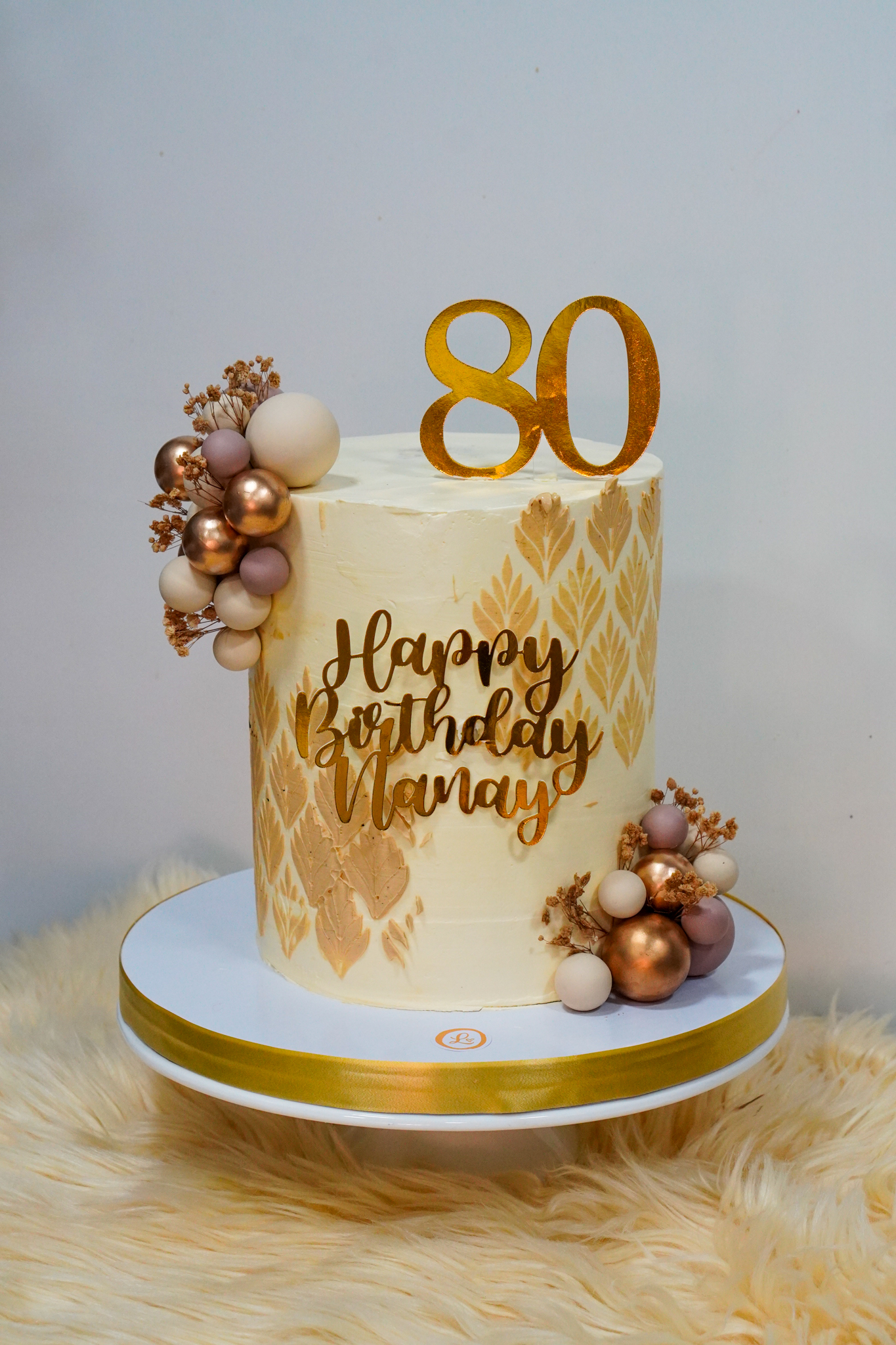 Elegant cream birthday cake with gold leaf pattern, balloon cluster decorations, and a gold 80 topper