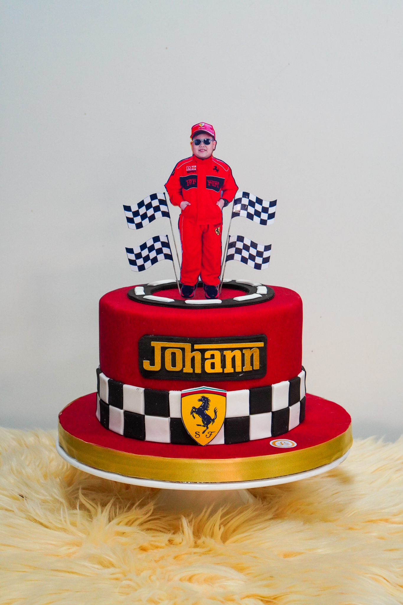 Ferrari-themed red birthday cake with checkered racing pattern, personalized name, and race car driver topper