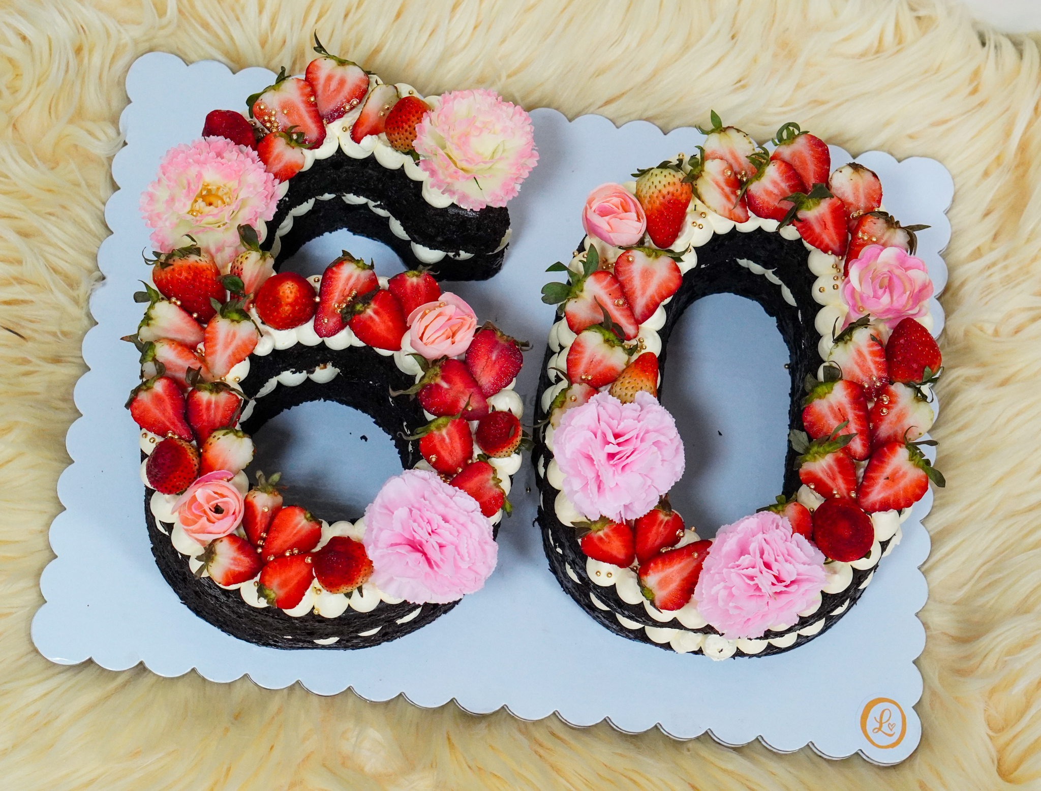Number-shaped chocolate cake in the form of 60, topped with fresh strawberries, pink flowers, and gold accents