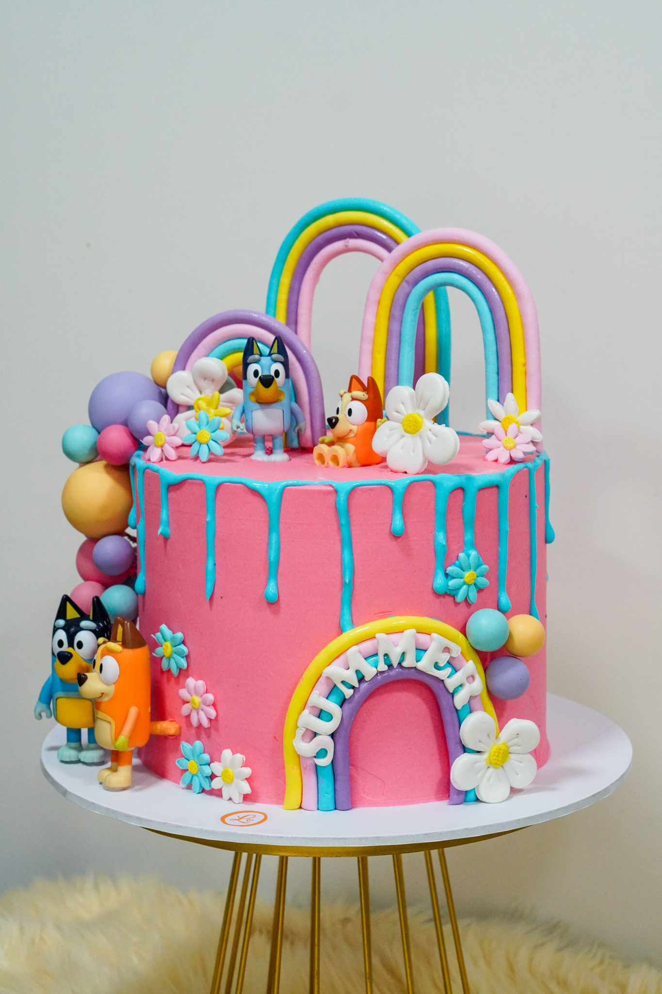 Bluey-themed pink birthday cake with rainbow toppers, balloon clusters, and flower decorations