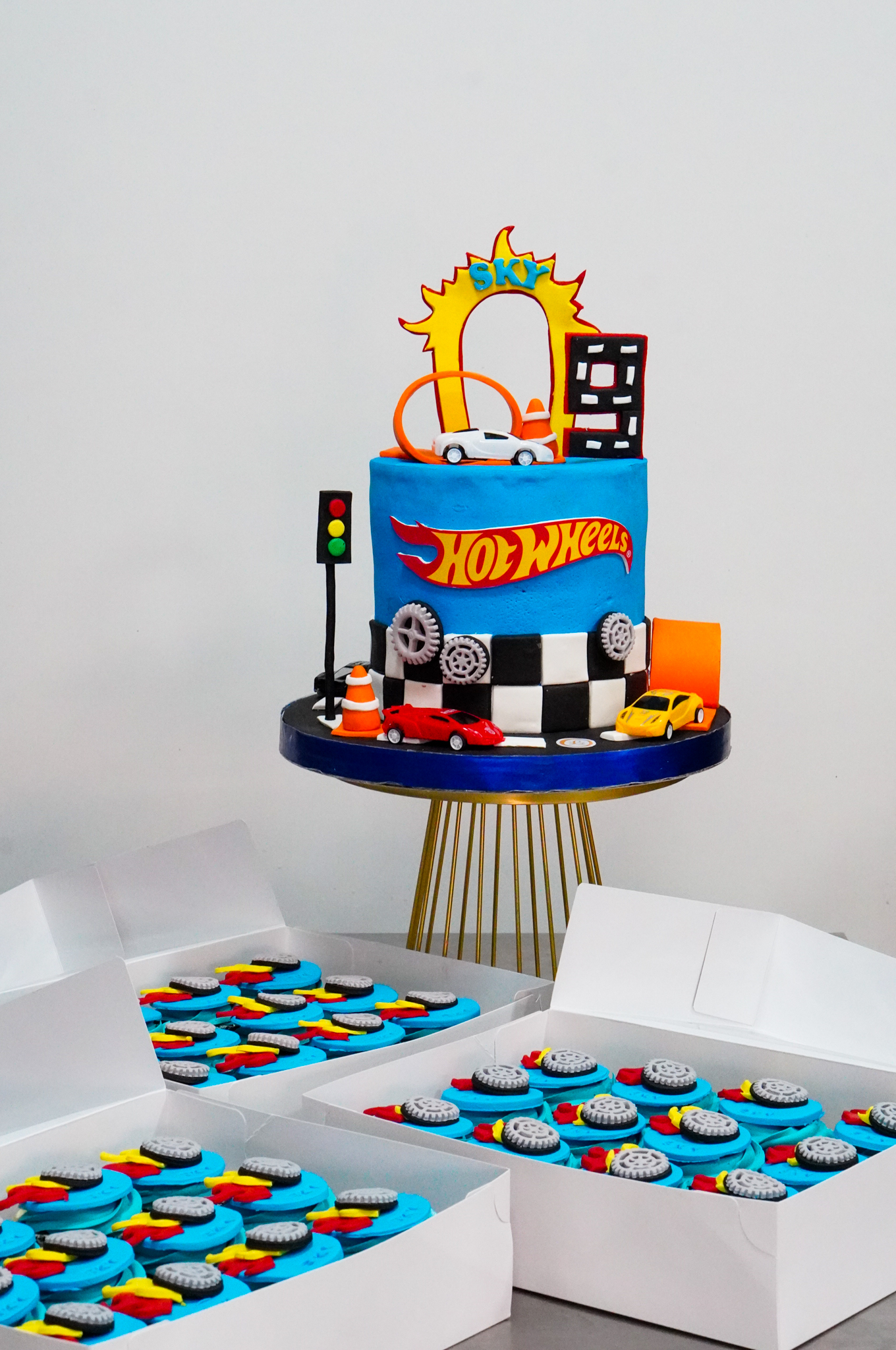 Hot Wheels-themed birthday cake with toy cars, racing track decorations, and matching cupcakes