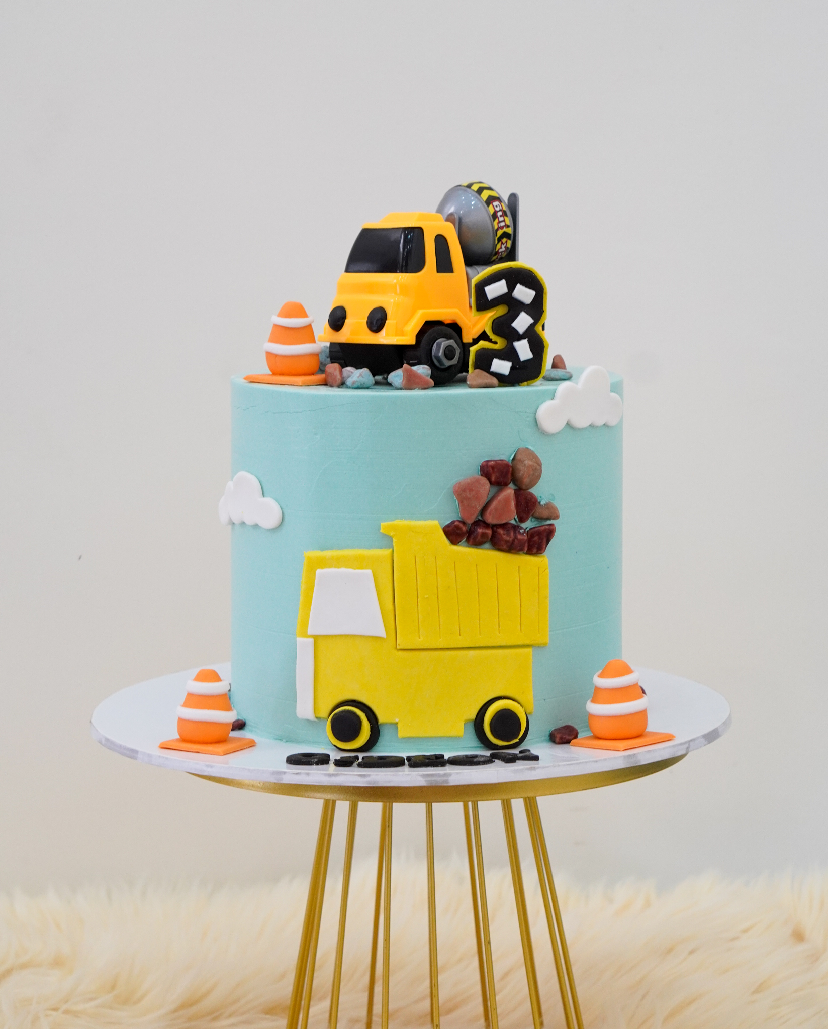 Construction themed blue buttercream cake with fondant cement mixer and dump truck, traffic cones, rocks, and clouds