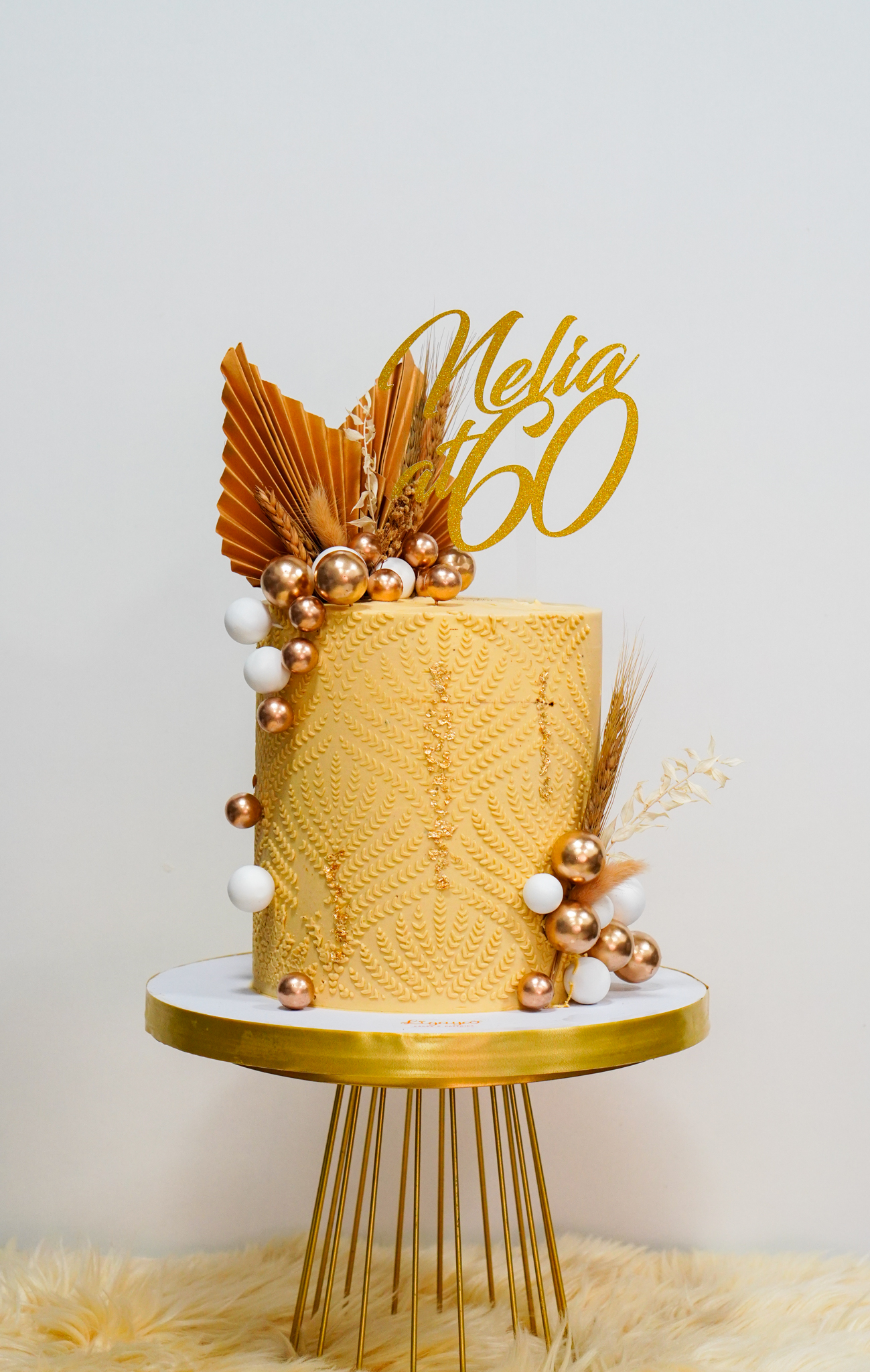 Elegant gold birthday cake with textured pattern, metallic spheres, dried floral accents, and a gold topper